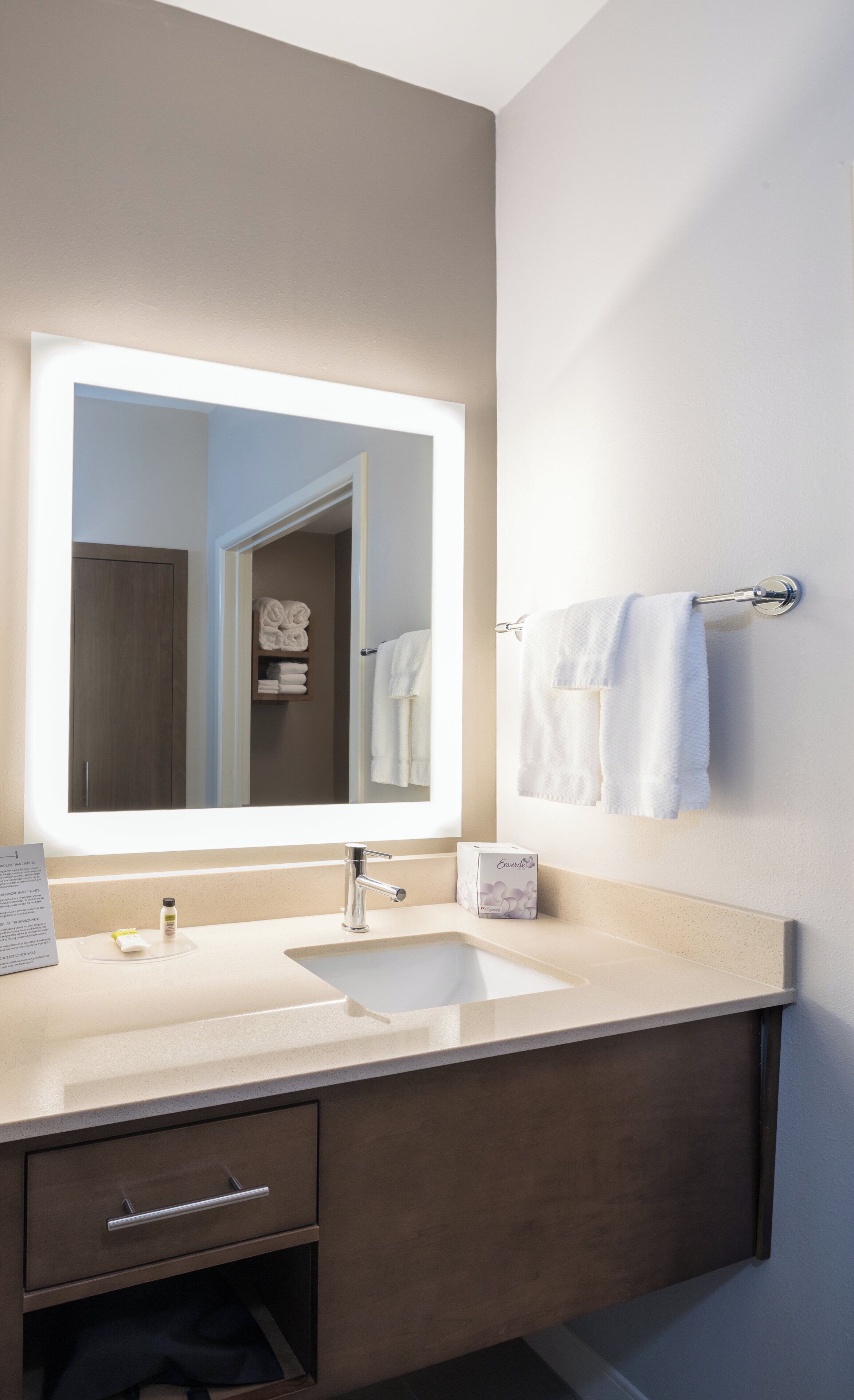 A modern bathroom with a large mirror, a sink, and a towel rack.
