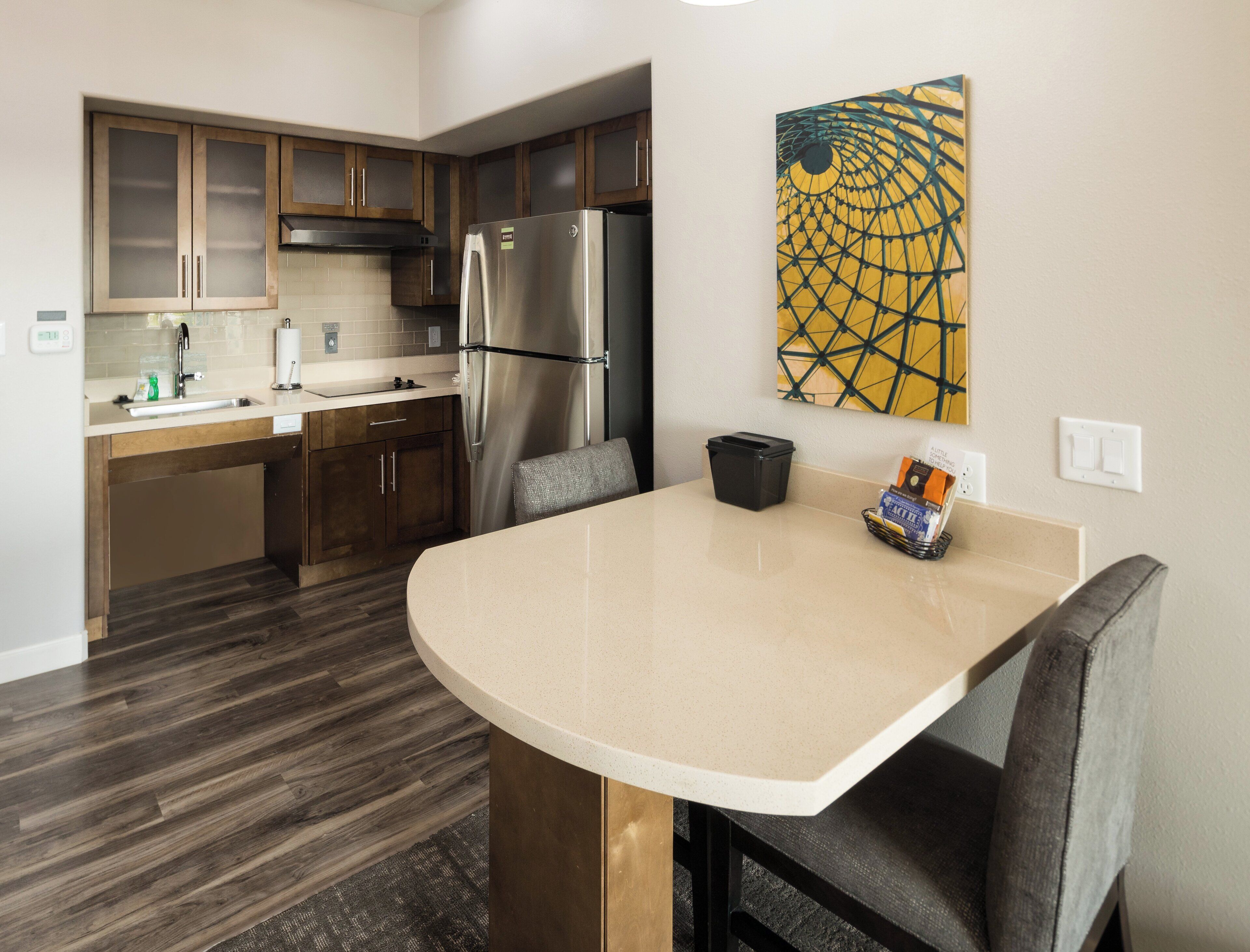 A modern kitchen with a stainless steel refrigerator, wooden cabinets, a built-in microwave, and a large island with bar stools.