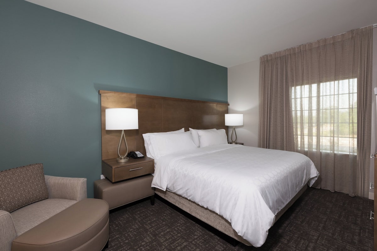 A hotel room with a large bed, two bedside tables with lamps, a sofa, and a window with curtains.