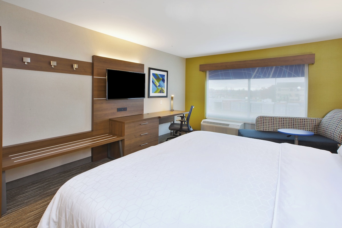Une chambre d’hôtel équipée d’un lit, d’un bureau, d’une chaise, d’une télévision et d’une fenêtre donnant sur un paysage agréable.