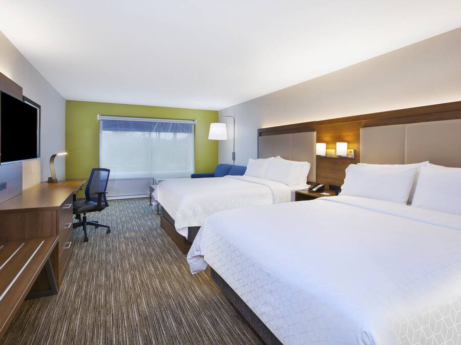 A hotel room with two beds, a desk, a chair, a TV, and a window with blinds.