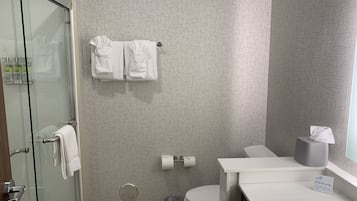 Un bagno moderno con parete a motivi geometrici, box doccia in vetro, WC e lavandino bianco con scatola per fazzoletti.