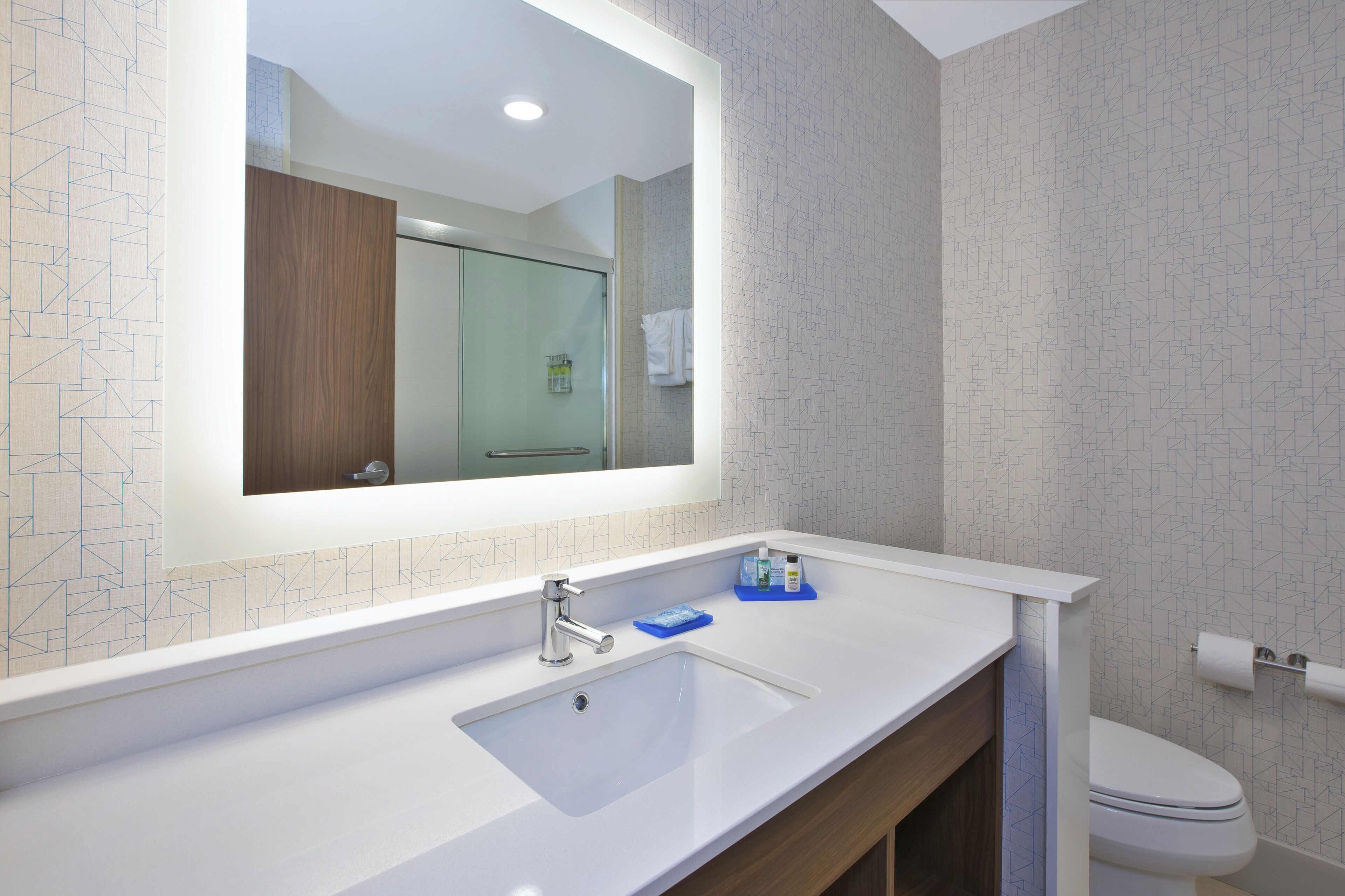 A modern bathroom with a large mirror, a white sink, and a toilet.