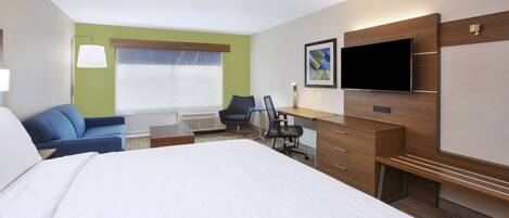 Habitación de hotel con una cama grande, un escritorio con silla, televisión y ventana con persianas.