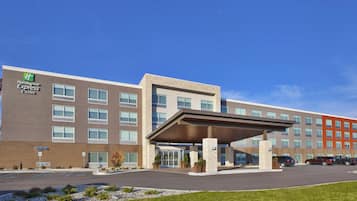 Edifício Holiday Inn Express & Suites com entrada coberta, estacionamento e céu azul claro.
