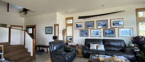 A spacious living room with a staircase, a black leather sofa, a wooden coffee table, and framed pictures on the wall.