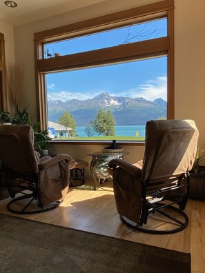 Una habitación con dos mecedoras mirando hacia una ventana grande con vistas a una montaña y un lago.