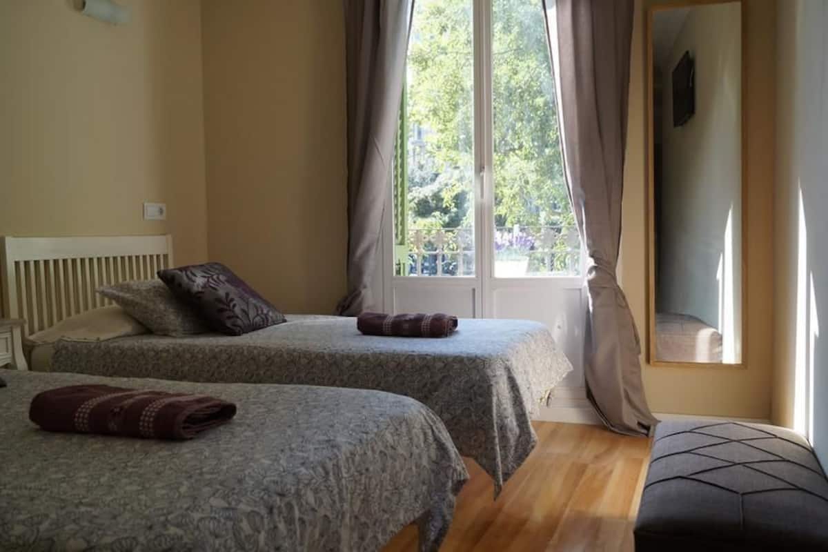 Un dormitorio con dos camas, una ventana con cortinas, un banco y un espejo.