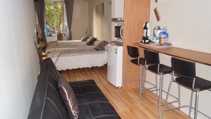 A compact room with a bed, a small kitchenette, and a seating area with a table and chairs.