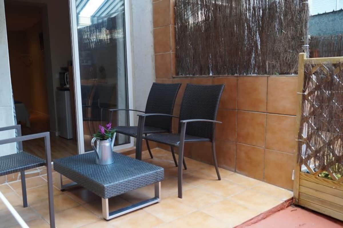 Un espacio al aire libre con un patio que tiene dos sillas, una mesita y una planta en maceta.