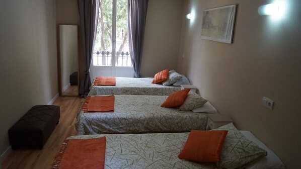 Une chambre avec trois lits, chacun agrémenté d’oreillers orange, un banc et un tableau au mur.
