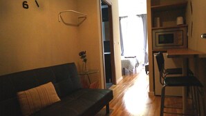 A living room with a dark sofa, a small table with a vase, and a kitchen area with a microwave and bar stools.