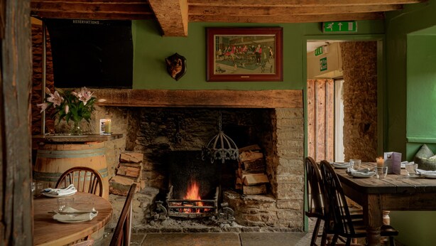 A rustic interior with a stone fireplace, wooden beams, a framed picture, and a green wall. - The Bell Inn (Lechlade)