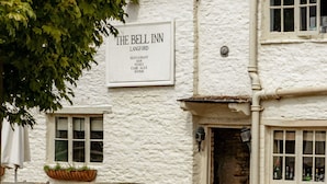 A white building with a sign reading 'The Bell Inn Langford' offering a restaurant, bar, wines, cask ales, and rooms. - The Bell Inn (Lechlade)