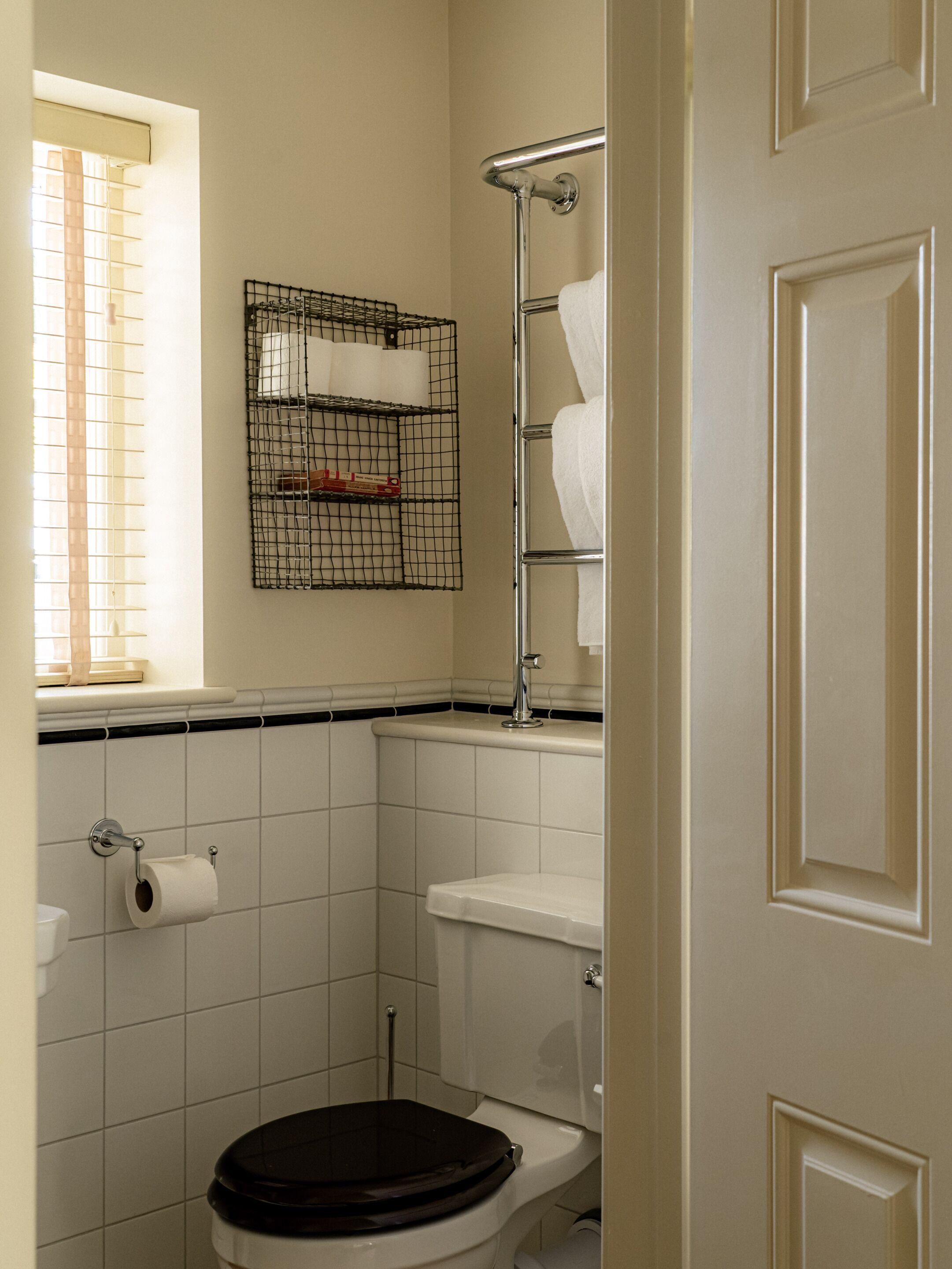 A bathroom with a toilet, a towel rack, a toilet paper holder, and a window with blinds.