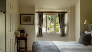 A bedroom with a bed, a window with curtains, a bedside table with a lamp, and a framed picture on the wall. - The Bell Inn (Lechlade)