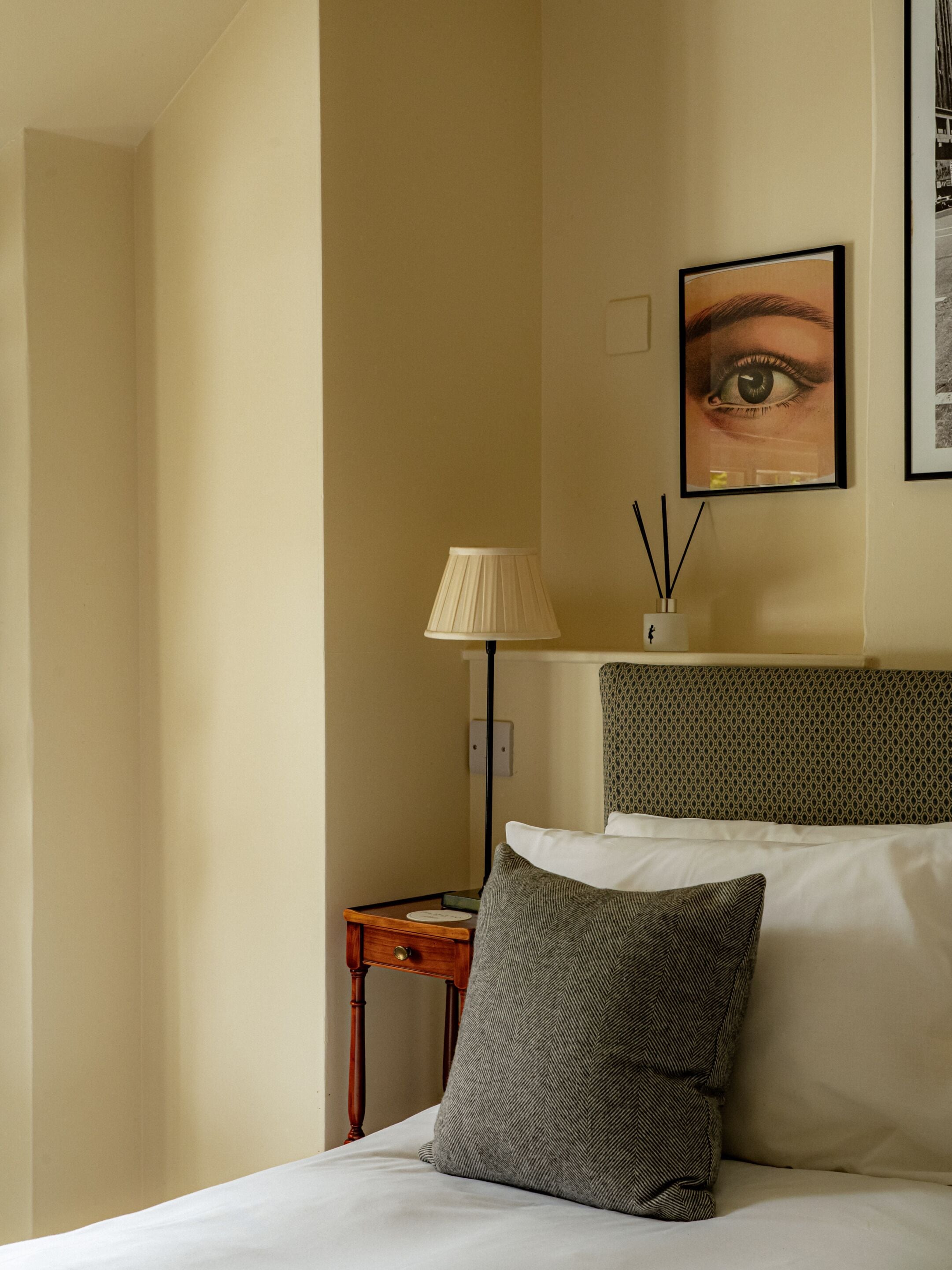 A hotel room with a bed, a bedside table, a lamp, a wall-mounted picture, and a patterned headboard.