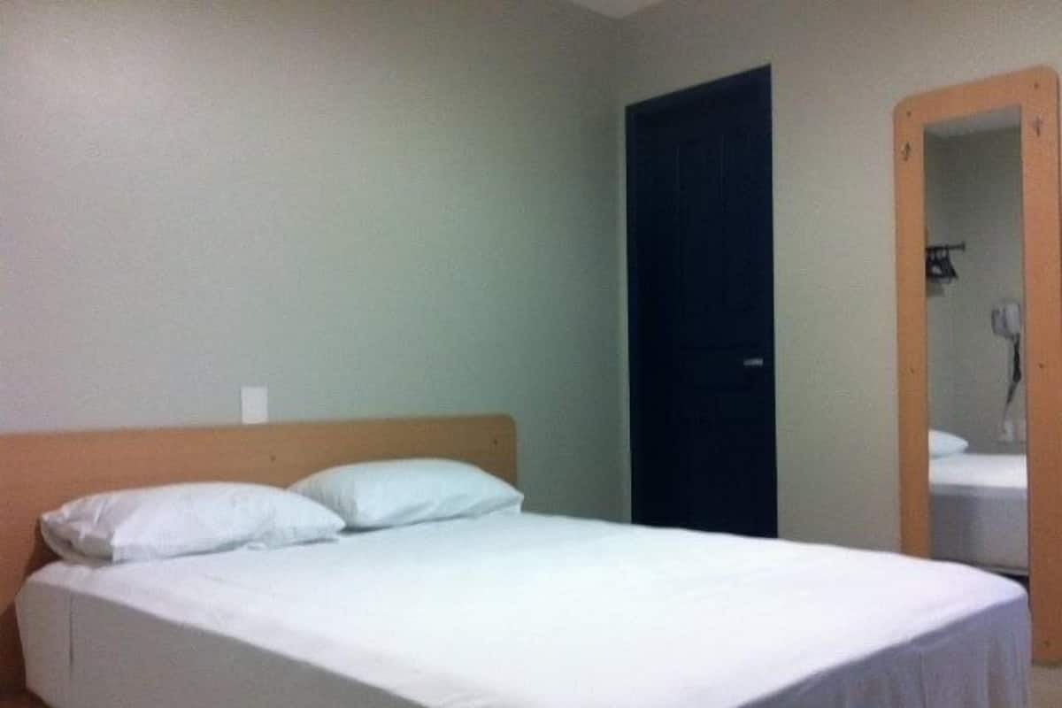 A single bed with white bedding in a room with plain walls and a dark door.