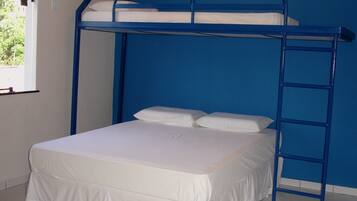 A bunk bed with a white mattress and pillows, a blue metal ladder, and a window with a view of greenery outside.