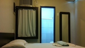 Ein Hotelzimmer mit einem Bett, einem Fenster mit Vorhängen, einem Spiegel und einem Wandheizkörper.