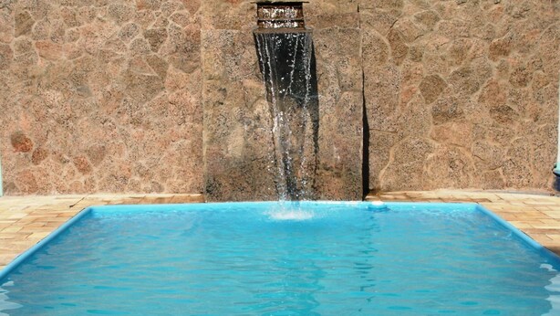Ein rechteckiger Pool mit klarem, blauem Wasser, einer Steinmauer und einem Wasserfall.