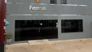 Ein Gebäude mit einer grauen Fassade und einem großen Eingang. Über dem Eingang ist ein Logo mit einem gelben 'F' und dem Text 'Ferrari Palace Hotel' zu sehen.