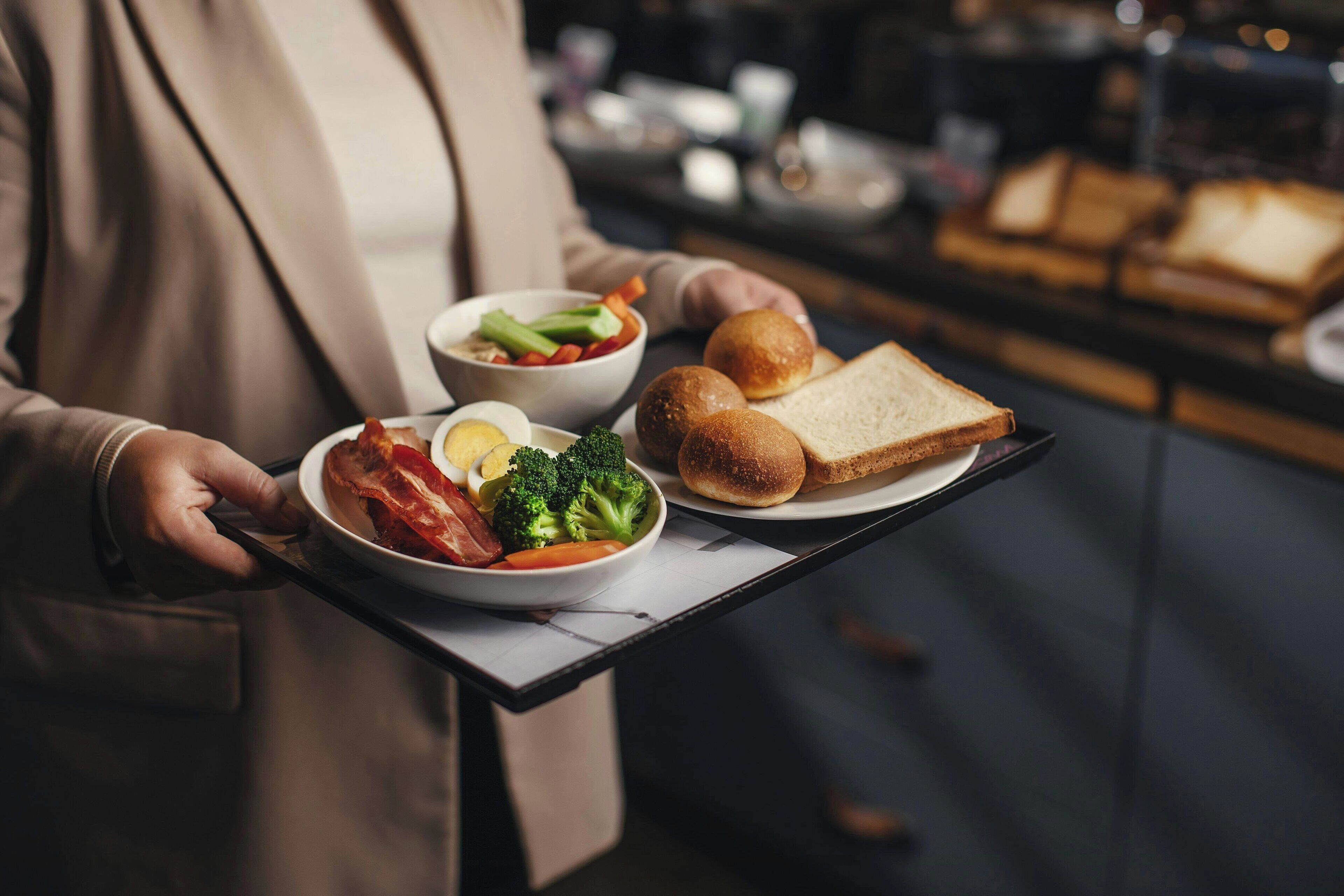 Una persona che tiene un vassoio con cibi per la colazione, tra cui pancetta, uova e toast.