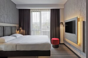 Habitación de hotel moderna con una cama grande, un televisor de pantalla plana en la pared y vistas al exterior a través de amplios ventanales.