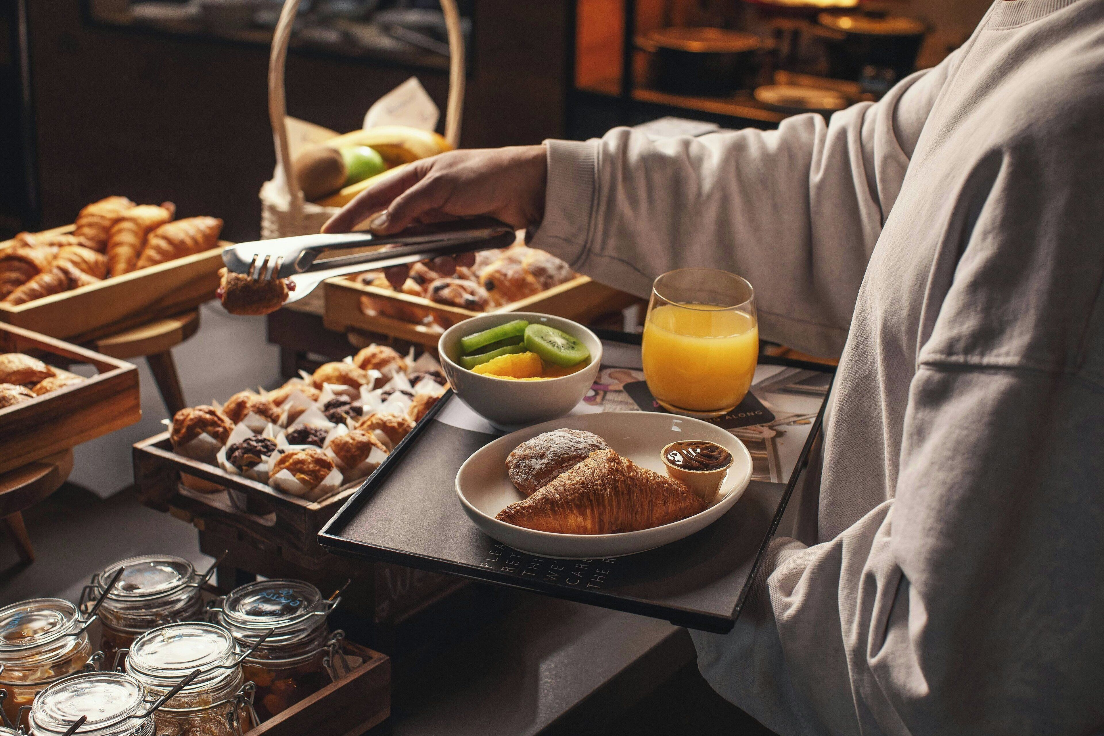 A breakfast tray with pastries, a bowl of fruit, and a glass of orange juice.