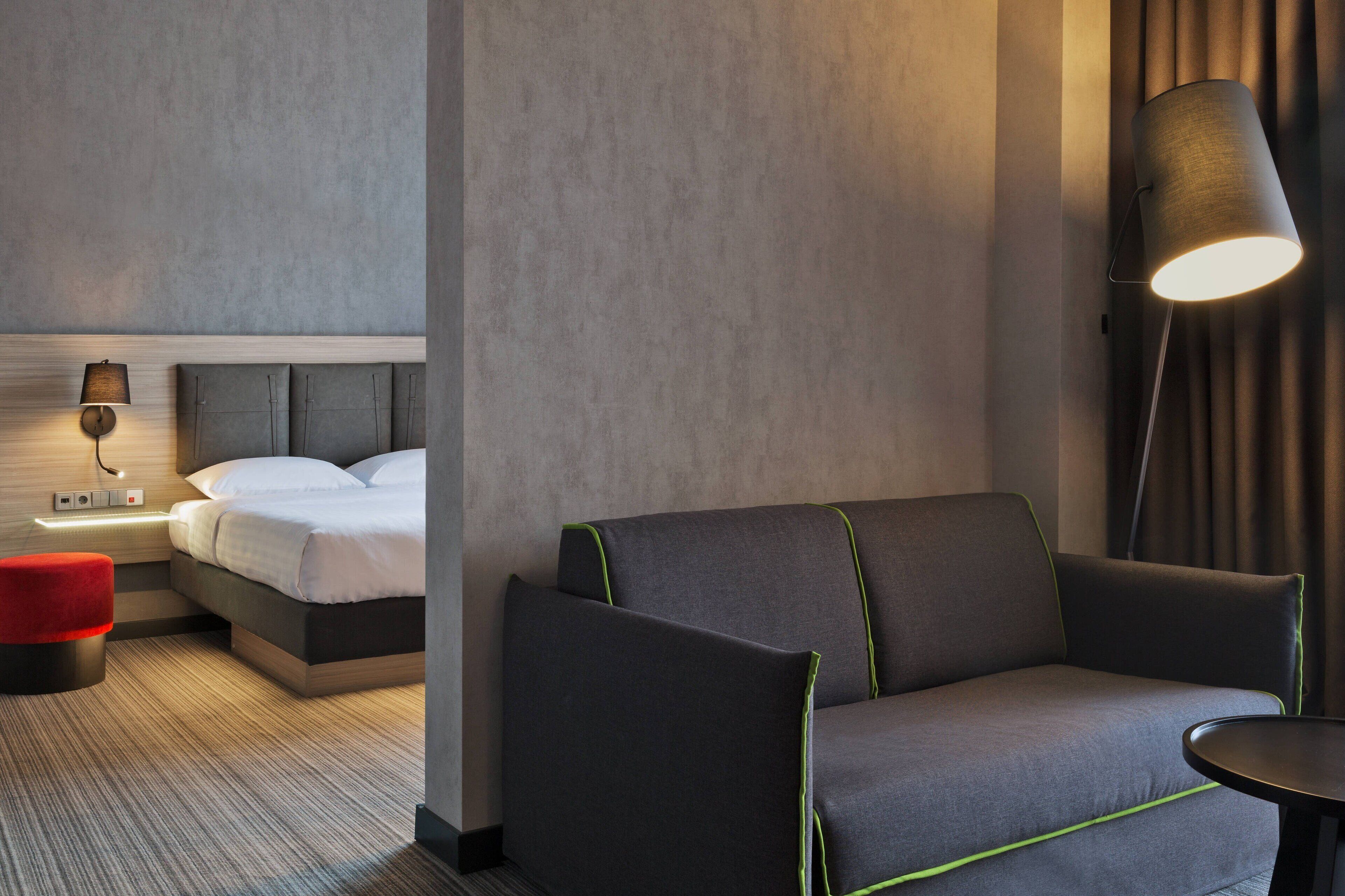 Ett modernt hotellrum med en s äng, en soffa, ett litet bord och en lampa.