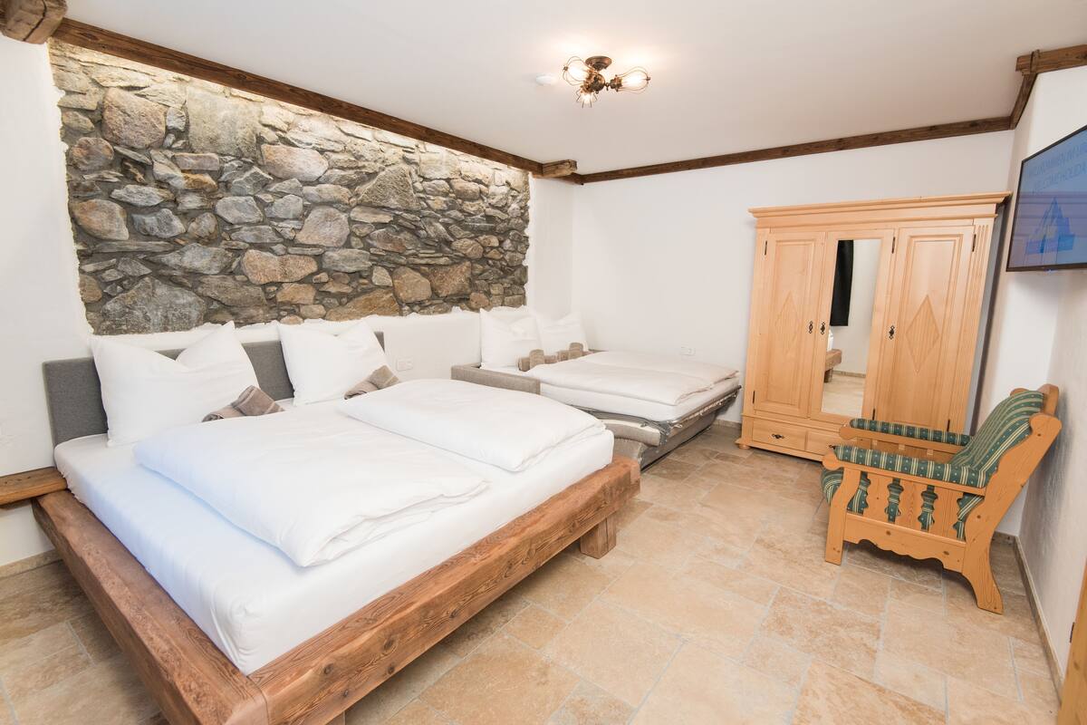 Quarto com parede de pedra, estruturas de cama de madeira, guarda-roupa de madeira e um banco.
