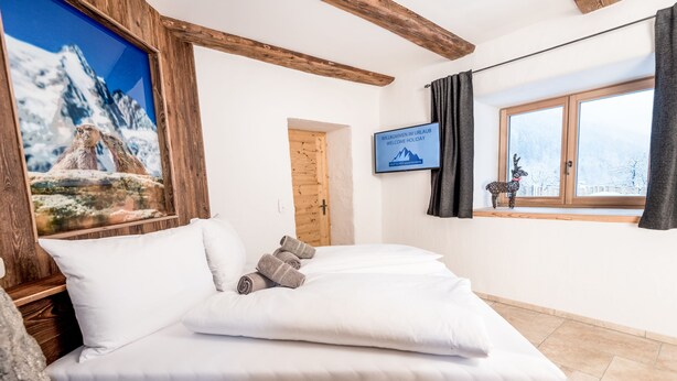 A cozy room with a bed, a wooden headboard, a framed picture of a mountain, a window with a view, and a welcome sign.
