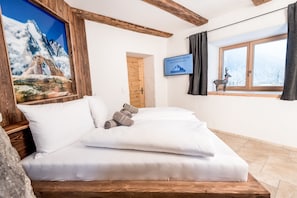 A cozy room with a bed, a wooden headboard, a framed picture of a mountain, a window with a view, and a welcome sign.