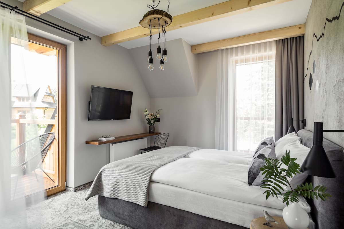 A modern bedroom with a bed, bedside lamp, and a TV on the wall.