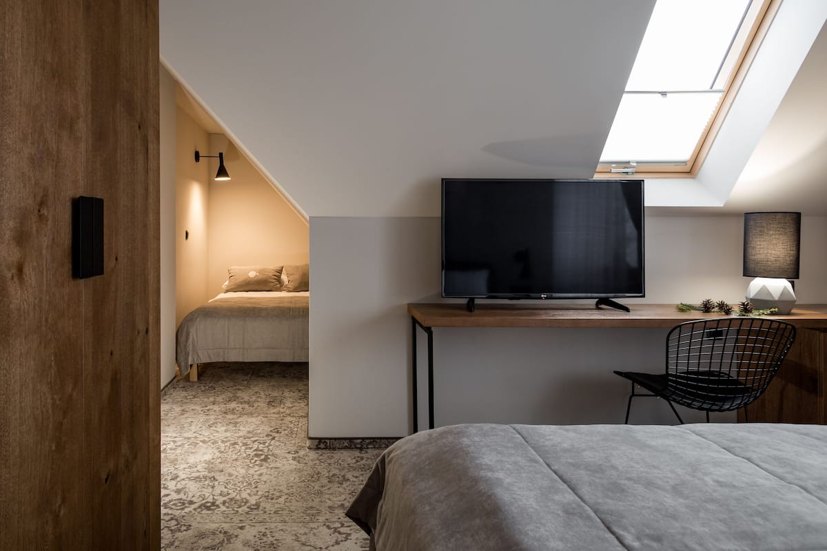 A modern loft bedroom with a skylight, a large flat-screen TV, a desk, and a comfortable bed.