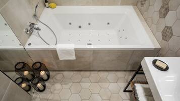 A modern bathroom with a large bathtub, a shower, and a toilet. There are hexagonal tiles on the floor and walls, and a towel is hanging on the wall.