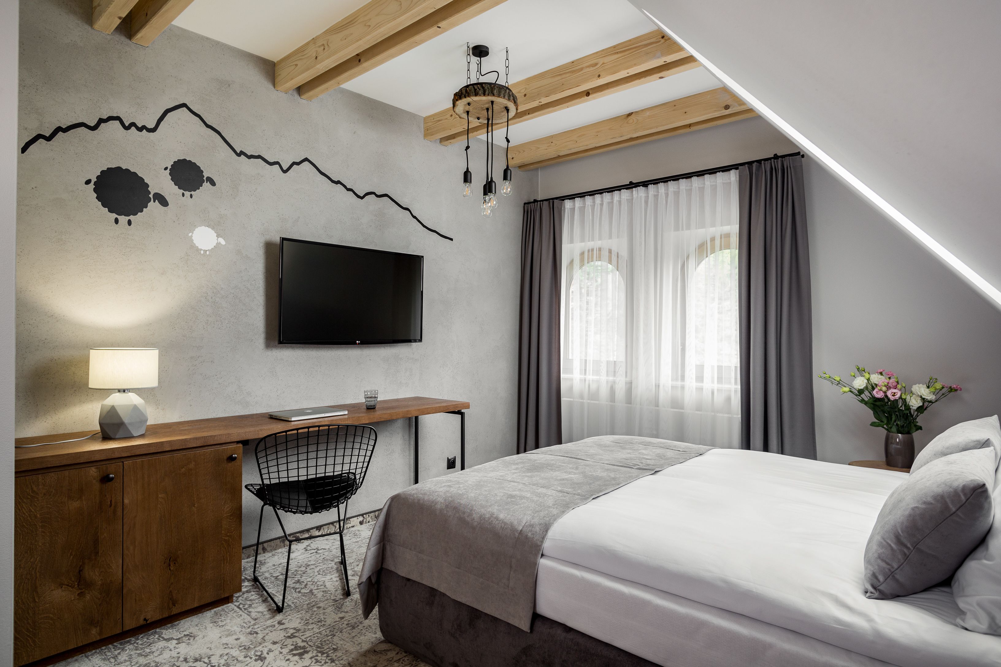 Un dormitorio con cama, escritorio, silla, televisor y una pared decorada con un diseño de montaña.
