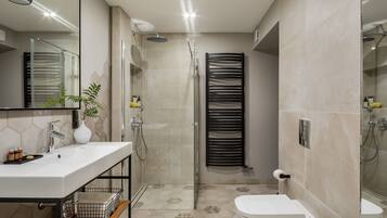 A modern bathroom with a large mirror, a white sink, a shower, and a toilet.