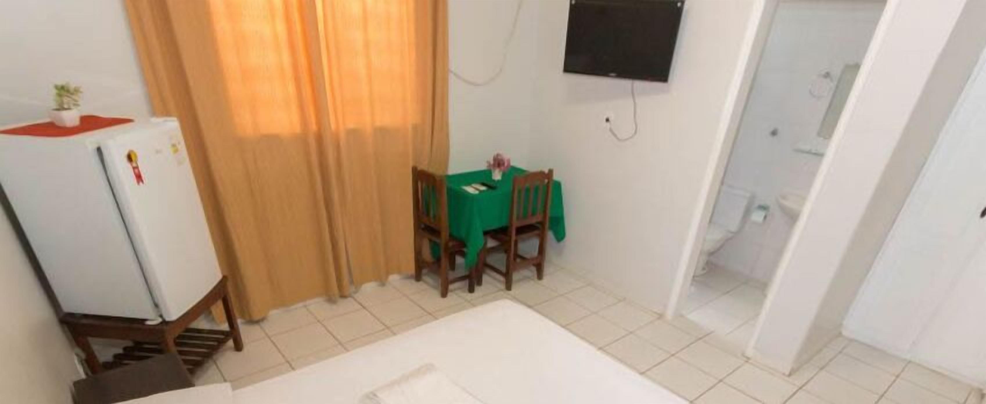 A small room with a bed, a table with chairs, a refrigerator, and a TV mounted on the wall.