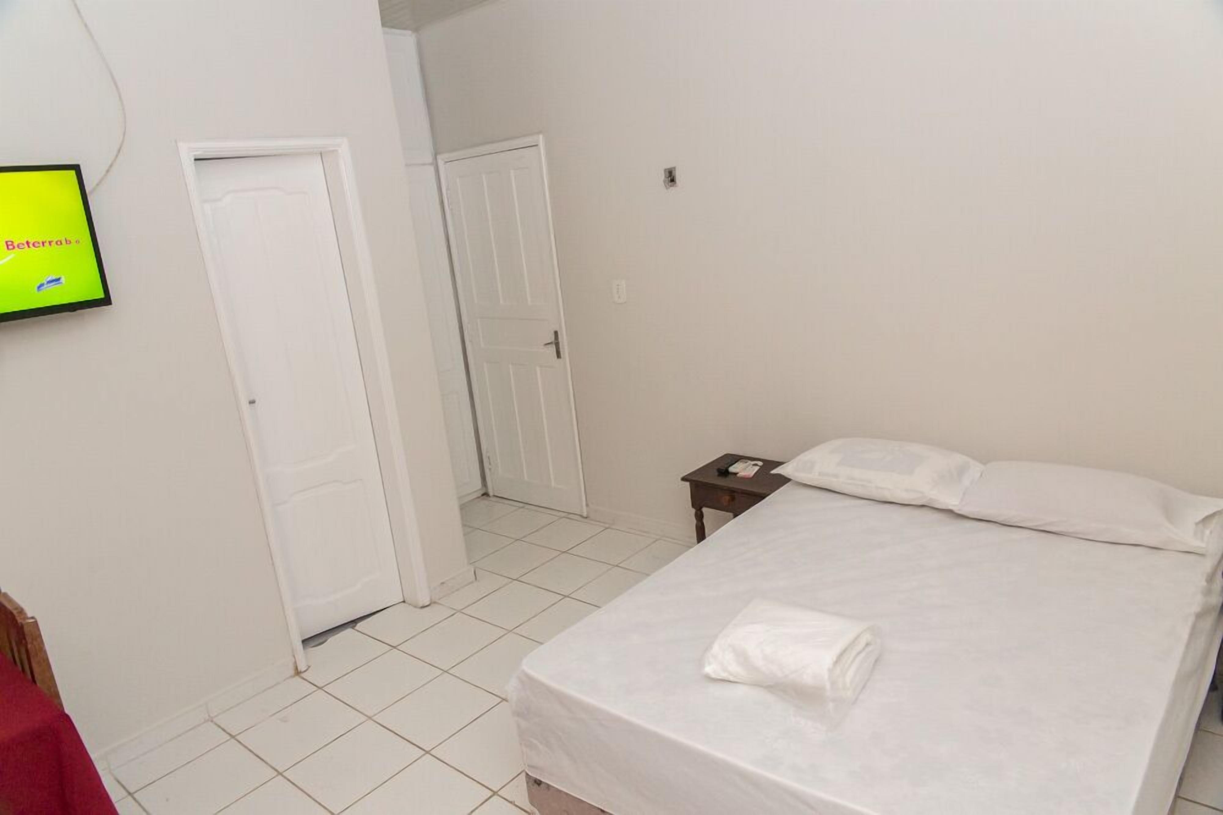 A hotel room with a bed, a nightstand, a TV, and a door leading to another room.