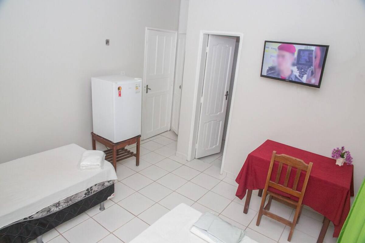 Una habitación pequeña con una cama, una mesa con mantel rojo y un televisor en la pared.