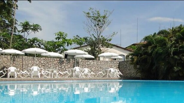 Ein Pool mit Liegestühlen und Sonnenschirmen, umgeben von Palmen und einer Steinmauer.