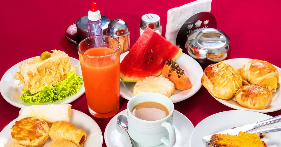 Una mesa con diferentes alimentos para el desayuno, como pasteles, un vaso de jugo de naranja, una tajada de sandía y una taza de café.