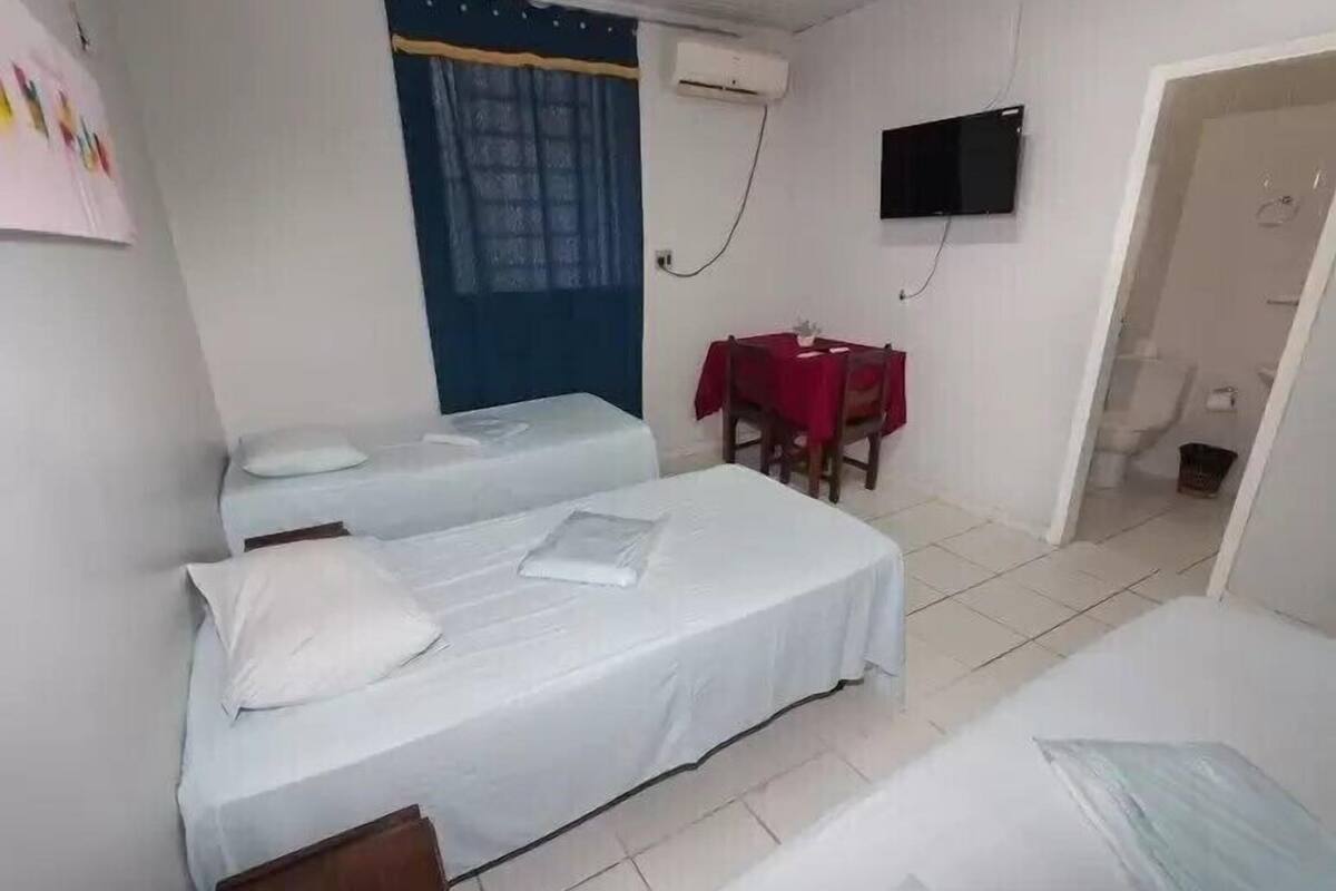 Una habitación con dos camas individuales, una mesita con mantel rojo, un televisor montado en la pared y un aire acondicionado.