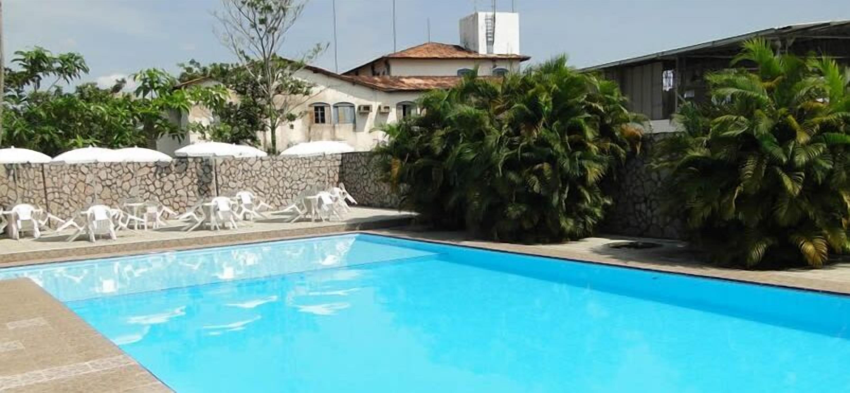 Piscina con sillas de descanso y sombrillas, rodeada por un muro de piedra y palmeras.