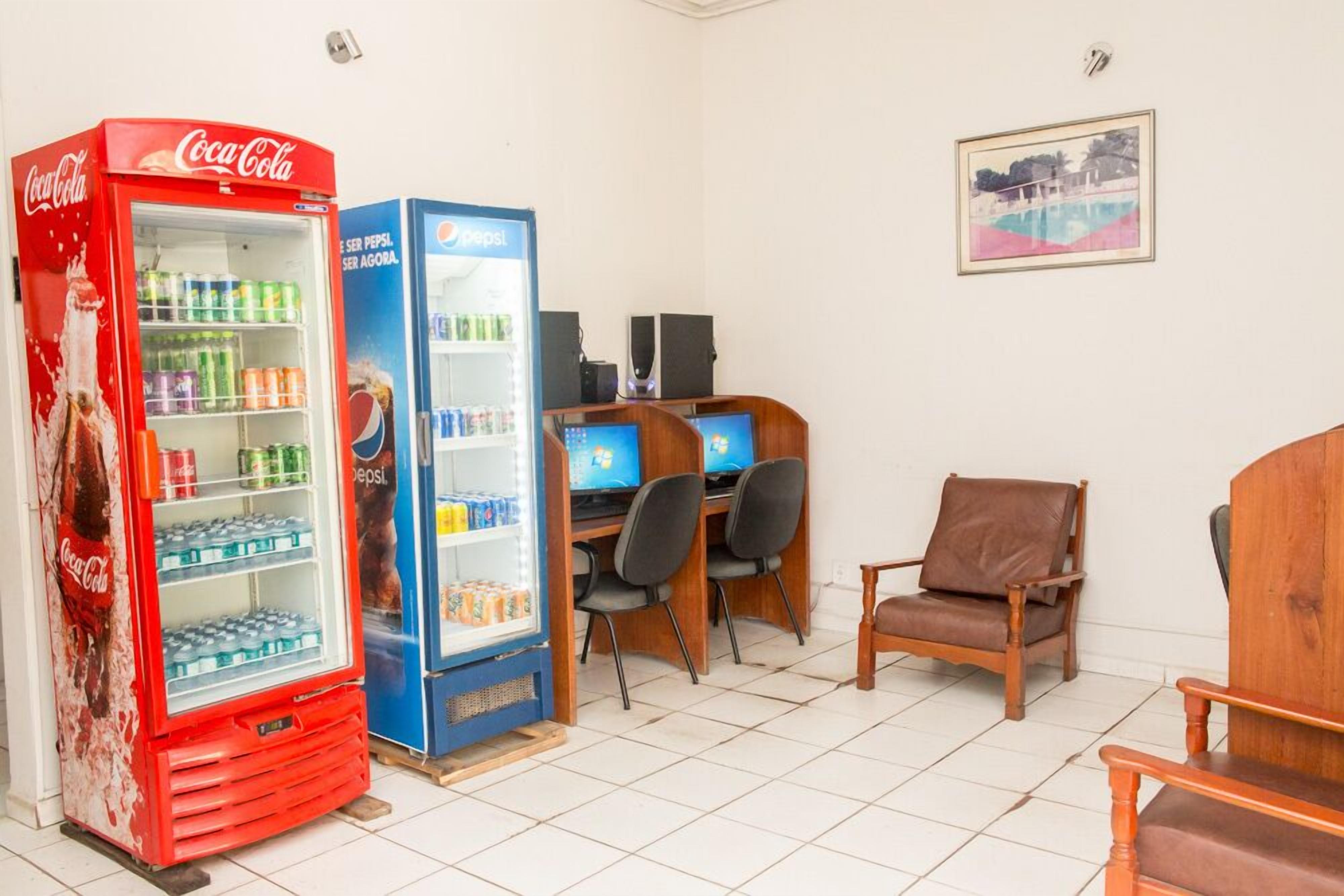 Una habitación con un refrigerador de Coca-Cola, un refrigerador de Pepsi, dos computadoras y una silla de madera.