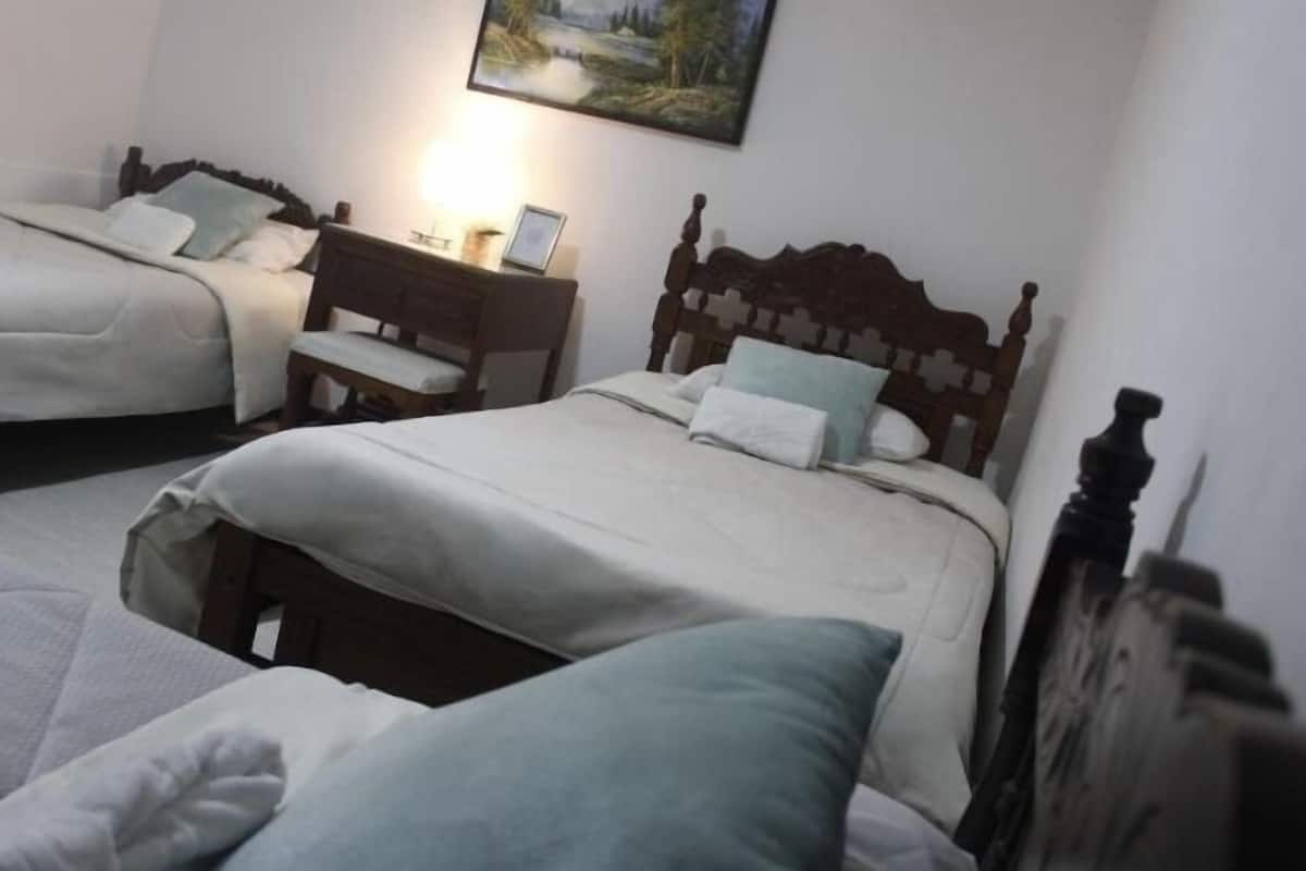 A room with two single beds, each with a wooden headboard and white bedding. There is a nightstand with a lamp and a framed picture on it.