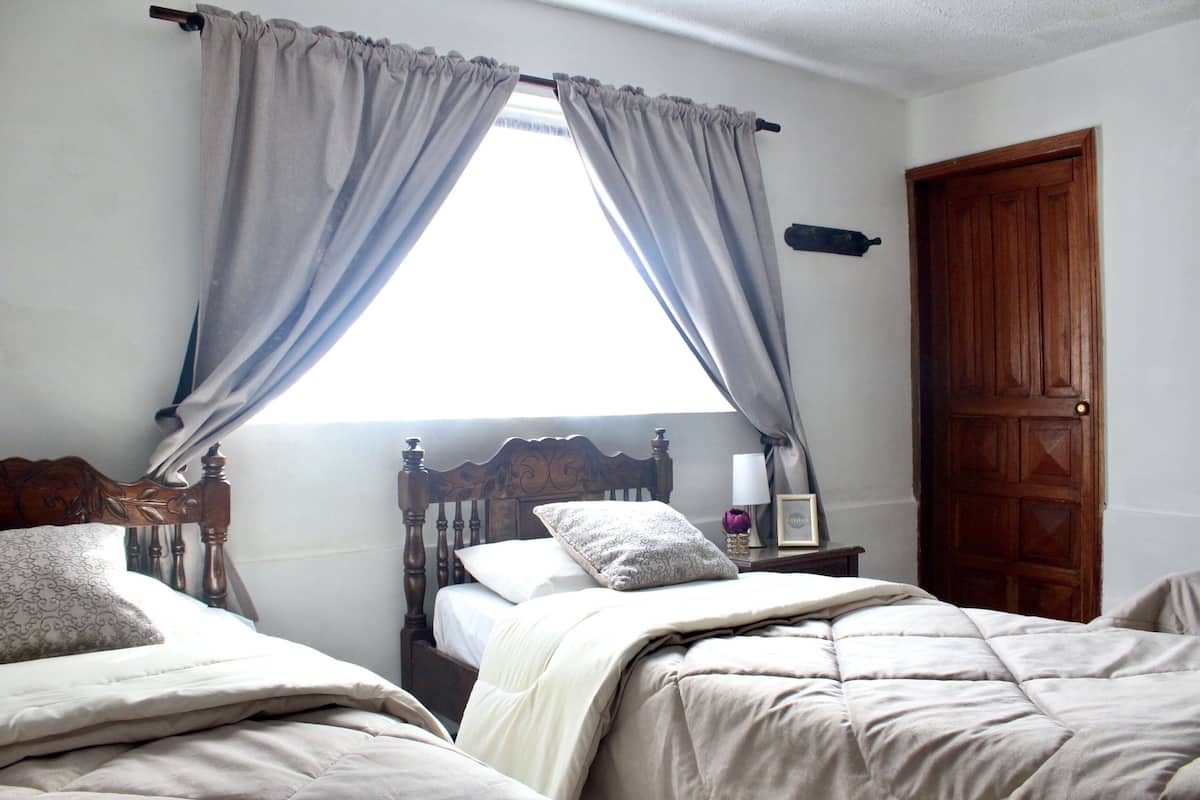 A bedroom with two beds, a wooden headboard, a nightstand, and a window with curtains.