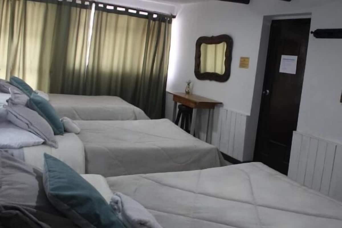 A hotel room with two single beds, a small table with a lamp, a mirror, and a door.