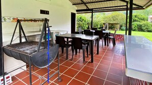 An outdoor covered patio with a grill, tables, and chairs. - Paraiso Cocora (Salento)